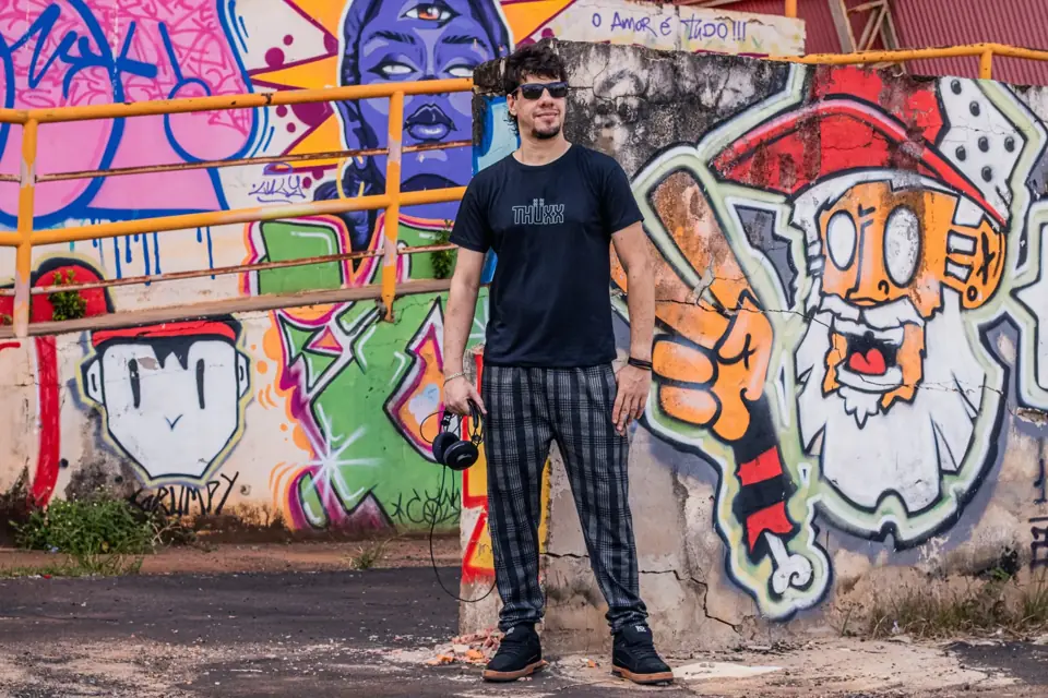 THUXX in front of a graffiti wall, holding headphones